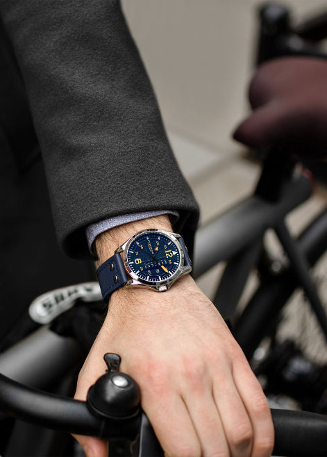 Hand wearing a watch with a blue strap on a blurred background