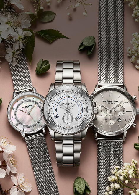 Three silver watches on a pink background with flowers and leaves.