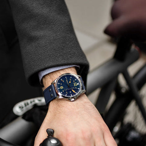 Hand wearing a watch with a blue strap on a blurred background