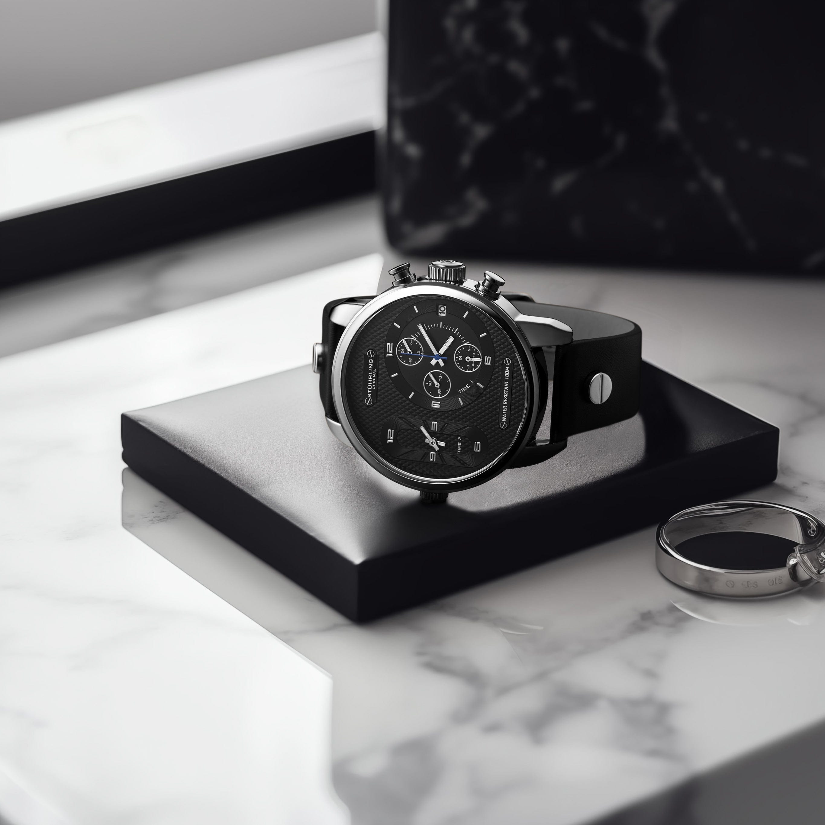 Black wristwatch on a white marble surface with a keychain.